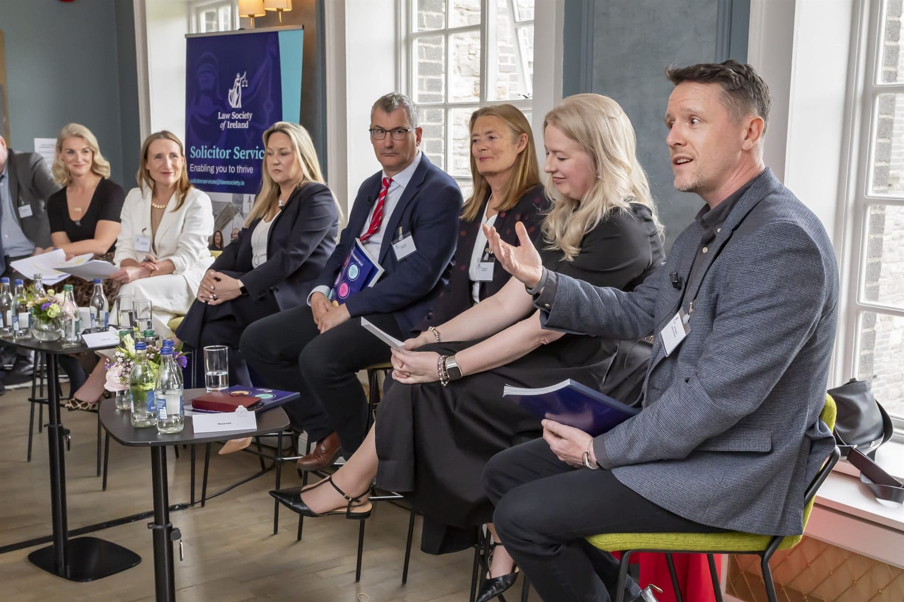 Ger Perdisatt speaking on a panel at a Law Society of Ireland event, alongside six other panellists in a bright Georgian room.